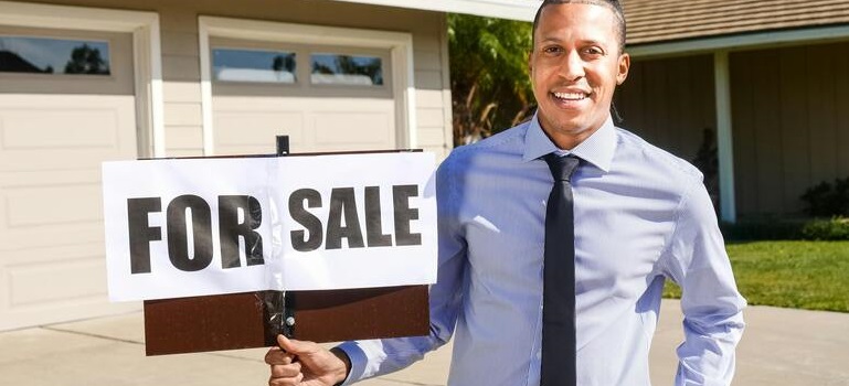 a realtor holding a for sale sign