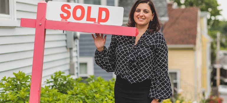 A woman next to the sold sign